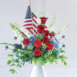 Red roses and blue-white flowers in a white vase with small American flags