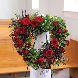 Heart-shaped red rose wreath on a stand with greenery