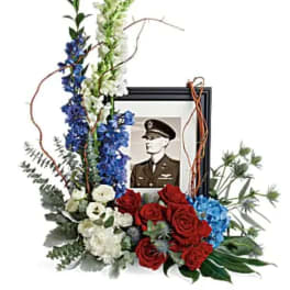 Floral tribute with a framed military portrait and red, white, and blue flowers