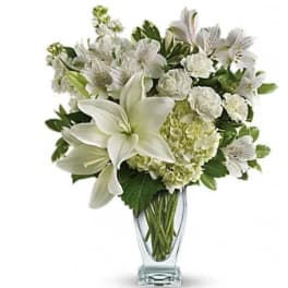 White lilies and mixed white flowers in a clear glass vase