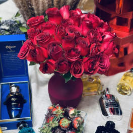Bouquet of red roses in a purple vase with perfume bottles and chocolate-covered strawberries