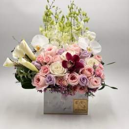 Pink and lavender roses with white orchids in a square box