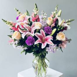 Mixed bouquet of pink lilies, roses, and purple flowers in a clear glass vase