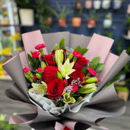 Bouquet of red roses, lilies, and pink carnations wrapped in gray and pink paper