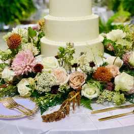 Four-tier white wedding cake surrounded by pastel flowers