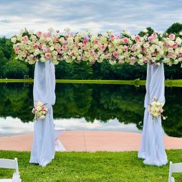 Floral wedding arch covered in pink and white roses with sheer white draping