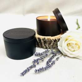 Black candle in a tin with a white rose and lavender sprigs beside it