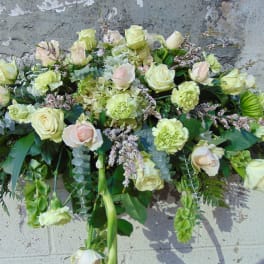 Long arrangement of cream roses and green carnations in a soft, cascading design