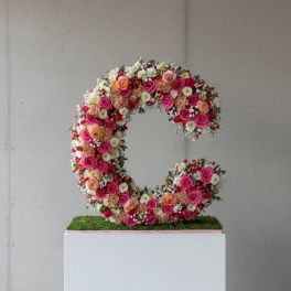 Floral letter C covered in pink, peach, and white flowers on a pedestal