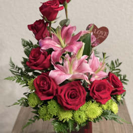 Red roses and pink lilies arranged in a red vase with a heart tag