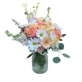 Pastel bouquet of peach roses, white daisies, and soft gerbera in a ribbed glass vase