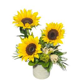 Three sunflowers arranged in a vase with greenery and raffia accents
