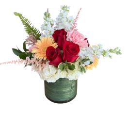 Mixed bouquet of red roses, white blooms, and pink flowers in a green vase
