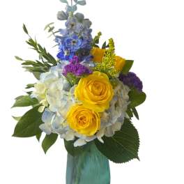 Yellow roses and blue hydrangeas in a teal glass vase