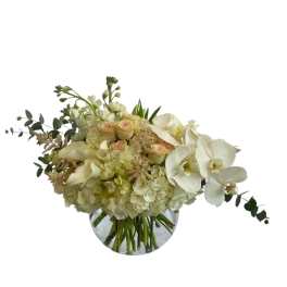 White floral arrangement in a round glass vase with orchids and hydrangeas