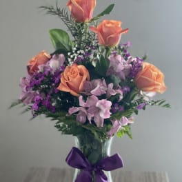Bouquet of peach roses and purple flowers in a glass vase with a purple ribbon