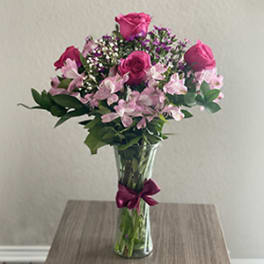 Pink roses and alstroemeria in a clear glass vase with a ribbon