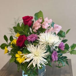 Mixed bouquet in a clear glass vase with red roses, white spider mums, and pink flowers