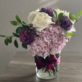 Pink hydrangea and white roses in a glass vase with purple blooms