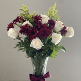 Bouquet of white roses and burgundy daisies in a glass vase with a ribbon