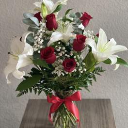 Bouquet of red roses and white lilies in a glass vase with a red ribbon
