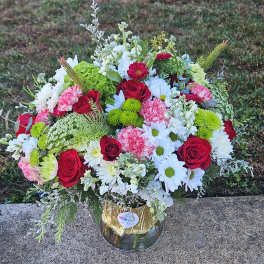 Mixed bouquet of red roses, white daisies, and pink carnations in a glass vase