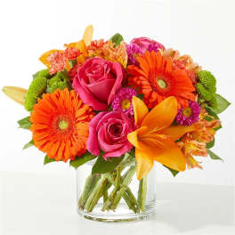 Bright bouquet of pink roses, orange gerberas, and yellow lilies in a glass vase