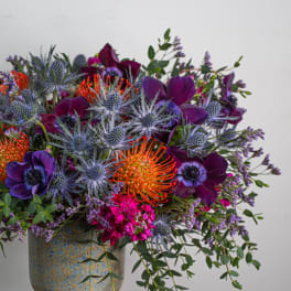 Colorful bouquet with purple blooms and orange pincushion flowers in a ceramic vase