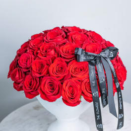 Round bouquet of red roses in a white vase with a black ribbon