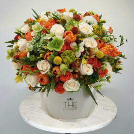 Mixed bouquet of orange, white, and green flowers in a white vase