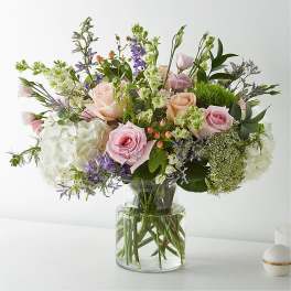 Pastel bouquet of pink roses, white hydrangeas, and mixed blooms in a clear glass vase.