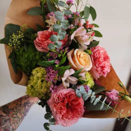 Hand-tied bouquet of pink and peach roses with mixed blooms wrapped in brown kraft paper