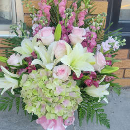 Pink roses and white lilies in a white vase with a pink ribbon