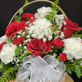 Red roses and white carnations in a white basket with a sheer bow