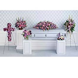 Floral funeral display with pink and purple arrangements around a white casket