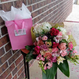 Pink and white mixed flower bouquet in a gift bag beside a brick wall
