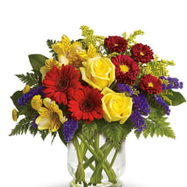 Bouquet of yellow roses, red daisies, and purple filler in a glass vase