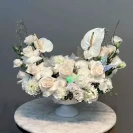 White floral arrangement in a pedestal vase with roses and anthuriums