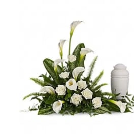 White calla lilies and roses arranged beside a white urn