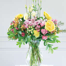 Mixed bouquet of yellow roses, pink blooms, and white flowers in a glass vase