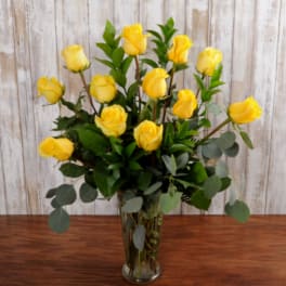 Yellow roses arranged in a clear glass vase with eucalyptus