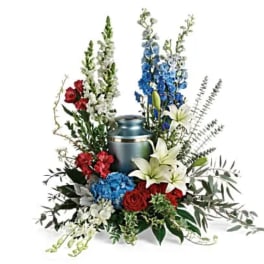 Sympathy arrangement with red, blue, and white flowers around a metal urn