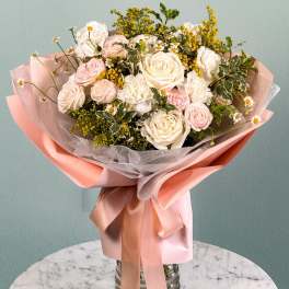 Bouquet of pale pink and white roses with small daisies wrapped in pink paper