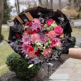Large bouquet of pink and purple flowers wrapped in dark paper
