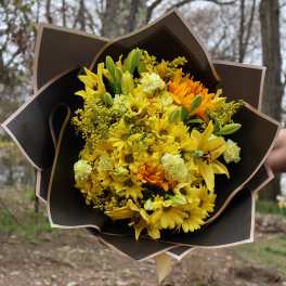 Yellow bouquet with lilies, daisies, and orange blooms wrapped in dark paper
