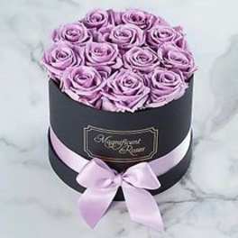 Lavender roses arranged in a black round box with a pink ribbon