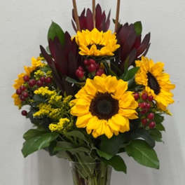 Bouquet of yellow sunflowers with dark burgundy flowers in a clear vase