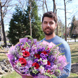 Man holding a large bouquet of purple and red flowers wrapped in pink paper