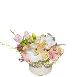 Low wedding centerpiece of white orchids, blush roses, and pastel tulips in a white vase