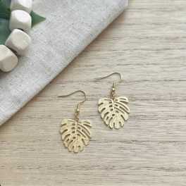 Pair of gold leaf-shaped dangle earrings on a wood surface